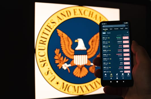 Kyiv, Ukraine - 06 June 2023: Man holds a smartphone with cryptocurrency quotes on Binance against the background of monitor with the SEC logo. S.E.C. Accuses Binance - fall of cryptocurrencies