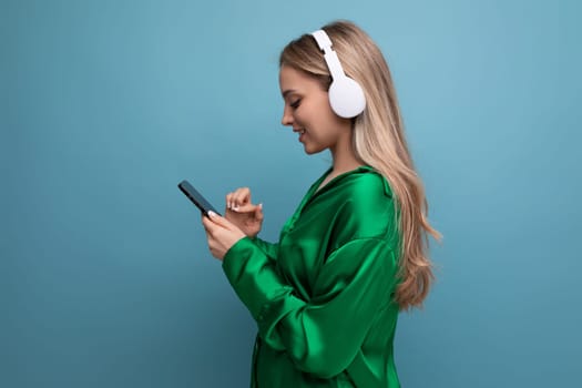 Profile photo of an attractive blond young adult woman in headphones on a blue background.