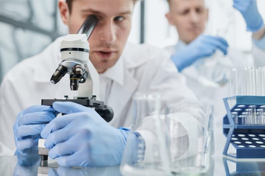 Young scientist or researcher in protective workwear studying new virus in microscope to develop antidote for fighting coronavirus