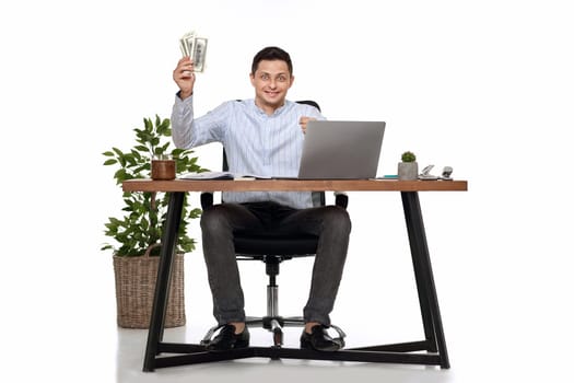 young freelancer man working on laptop and holding money while sitting on chair at desk.