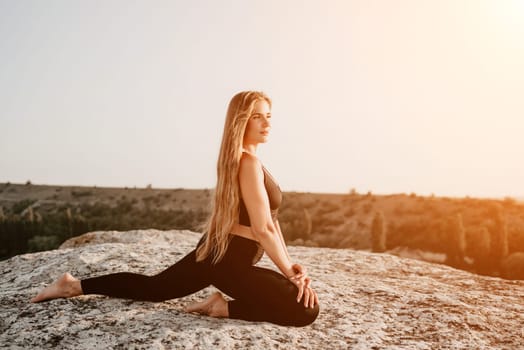 Well looking middle aged woman with long hair, fitness instructor in leggings and tops doing stretching and pilates on the rock near forest. Female fitness yoga routine concept. Healthy lifestyle.