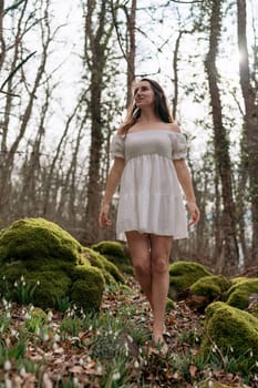 Snowdrops galanthus woman. She stands in a white dress on a meadow with snowdrops in a spring forest.