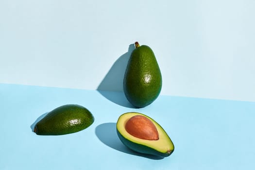 Composition of fresh fruits, whole avocado and two halfs of cutted avocado on blue background. Mock up, two-colored pastel