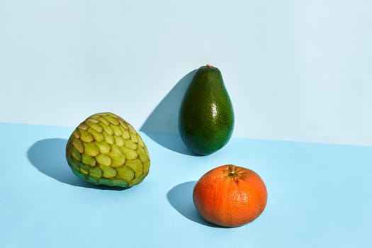 Composition of fresh fruits, cherimoya , sugar-apple, fruit of annona squamosa and avocado on blue background. Mock up, two-colored pastel