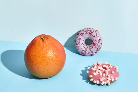 Composition of fresh fruits and sweets, two donuts and juicy grapefruit on blue background. Mock up, two-colored pastel