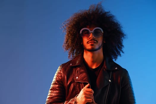 Portrait of a stylish man with curly hair with glasses smile on blue background multinational, color light, black leather jacket trend, modern concept. High quality photo
