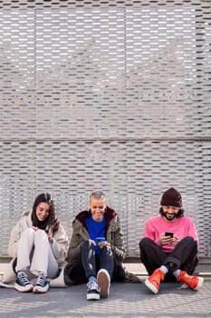 three young friends sitting in the floor scrolling together through social media with mobile phone, concept of friendship and modern lifestyle, copy space for text