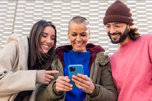 three young friends smiling happy and enjoying the moment using together a mobile phone, concept of technology of communication and modern lifestyle