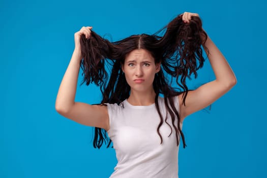 Sad woman is pulling her hair on the blue background