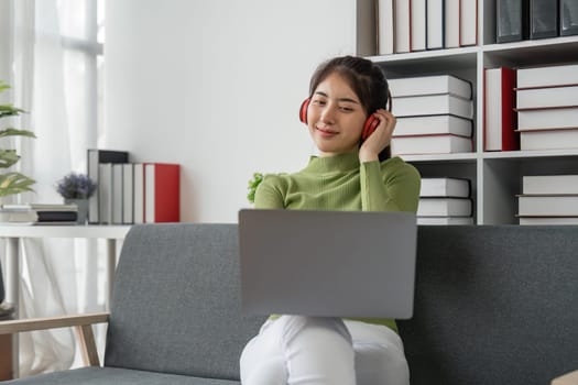 Beautiful young asian woman choose music from laptop take a rest and listening song with headphone. Lifestyle in living room at house in the morning. Relaxing time in living room.