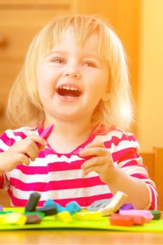 Cute laughing llittle girl playing with plasticine at home
