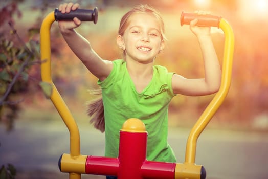 Little girl does exercises at simulator in park