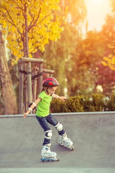 Little girl on roller skates in helmet at a park at sunset