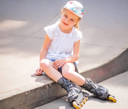 Little girl sitting with roller skates in park