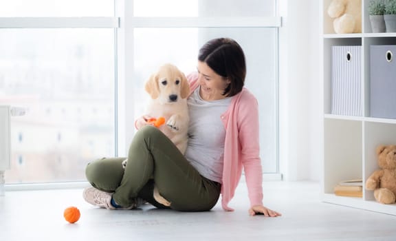 Pretty woman playing with retriever puppy indoors