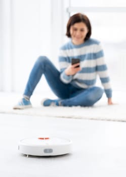 Woman managing automatic vacuum cleaner via smartphone