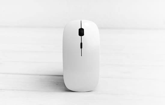 Wireless computer mouse standing vertically on white wooden table