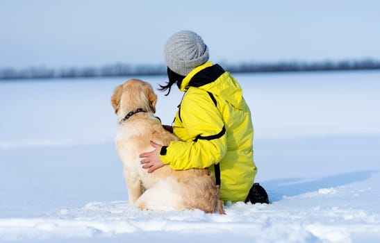 Rear view of friendly dog and woman sitting on snowy field