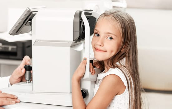 Happy little girl at ophthalmological clinic with modern equipment