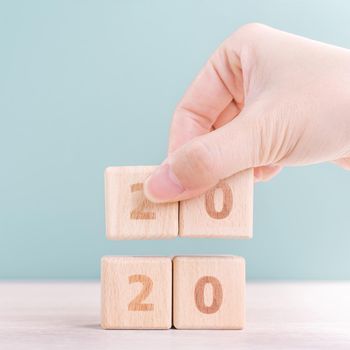 Abstract 2020 & 2019 New year countdown design concept - woman holding wood blocks cubes on wooden table and green background, close up, copy space.