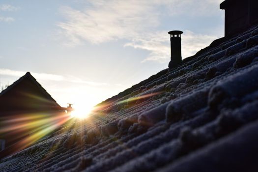 Sunrise over a frozen roof with moss against a blue sky with few clouds