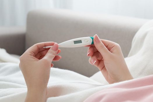 Woman looking at thermometer. Female hands holding a digital thermometer. Girl measures the temperature. Concept of fever, flue or virus
