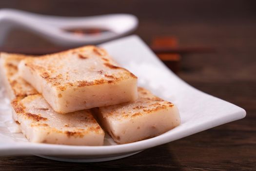 Delicious turnip cake, Chinese traditional local dish radish cake in restaurant with soy sauce and chopsticks, close up, copy space.