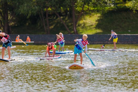 A child swims on a surfboard, pushing off with a paddle. Paddleboarding. Russia Zelenograd 14 August 2021