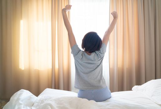 Woman stretching in bed after wake up, back view