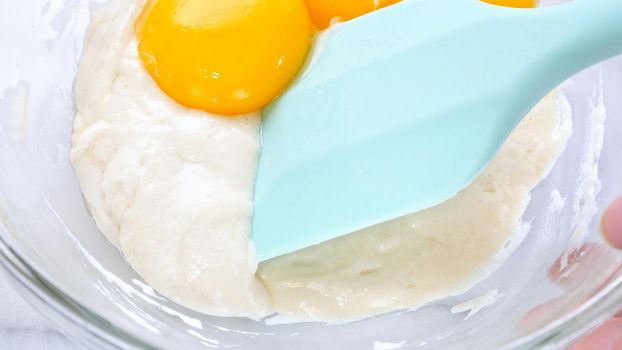 Mixing egg yolk into cake batter with green rubber spatula mixer tool stirring until smooth and blend well in a glass bowl, close up, lifestyle