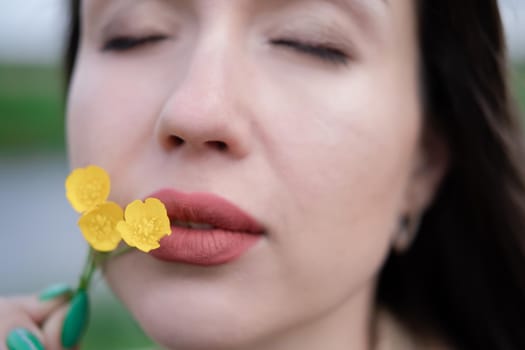 portrait of beautiful brunette woman with yellow small wildflower. skin care, nature.