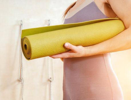 Woman wearing activewear standing in gym holding yoga mat ready start fitness or yoga training. Concept of sports lifestyle. Yoga concept