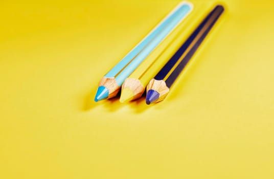 Three wooden colored pencils on yellow background