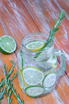 Glass with fresh organic detox cucumber water with lime and lemon on wooden background.
