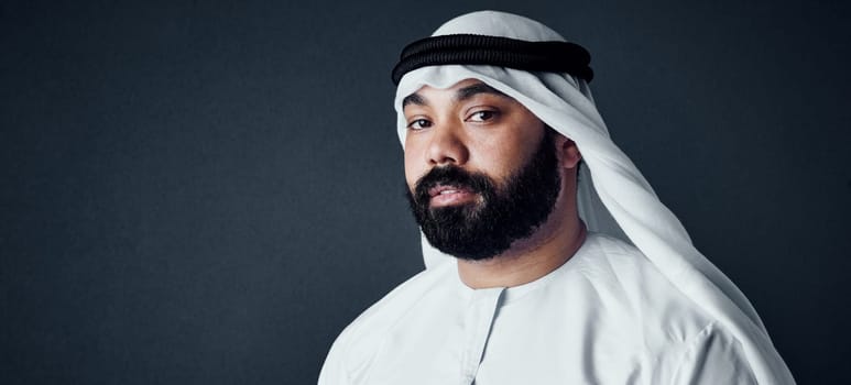 He loves the traditional look. Studio shot of a young man dressed in Islamic traditional clothing posing against a dark background