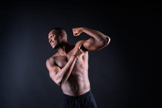 Athletic african american man topless, big muscles, a dark background studio