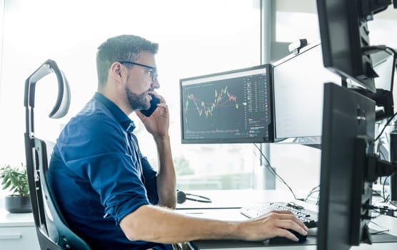 Male stock broker trading online watching charts and data analyses on multiple computer screens.