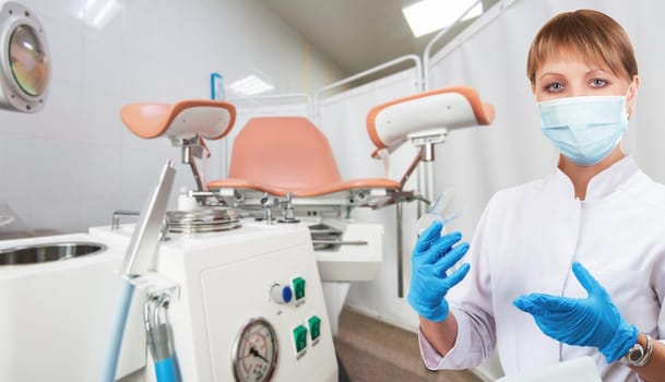 Female gynecologist in protective mask and whitecoat with gynecological vaginal retractor in hand