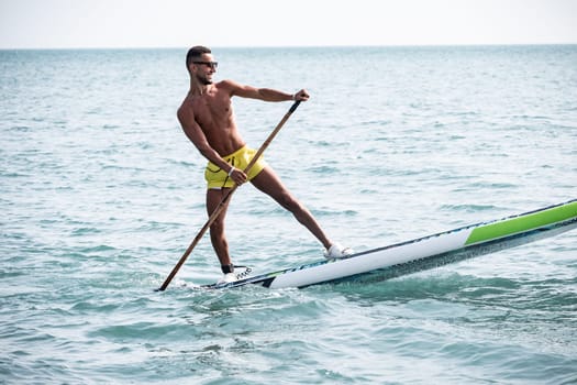 a sporty guy swims on a sup board with a paddle on the sea during the day against a beautiful sky in summer