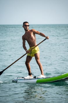 a sporty guy swims on a sup board with a paddle on the sea during the day against a beautiful sky in summer