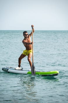 a sporty guy swims on a sup board with a paddle on the sea during the day against a beautiful sky in summer