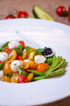 salad with avacado, mozzarella and tomatoes in a white plate.