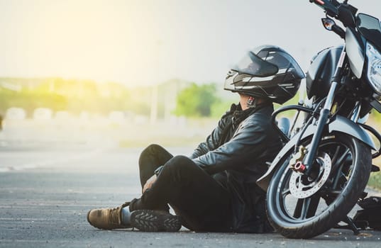 Biker sitting next to his motorcycle on the road. Male motorcyclist sitting and leaning on his motorcycle on the asphalt