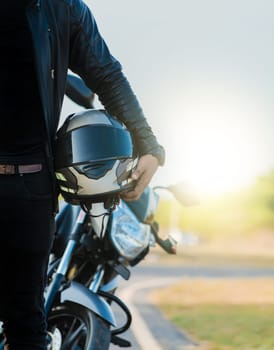 Motorcycle safety helmet concept. Unrecognizable biker holding helmet next to motorbike near the road. Motorcyclist holding safety helmet next to his motorbike near the road