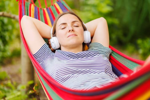 Young woman in headphones listening to music while resting in hammock outdoors.