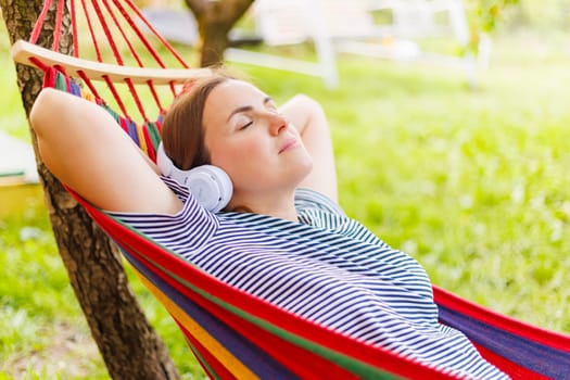 Young woman in headphones listening to music while resting in hammock outdoors.