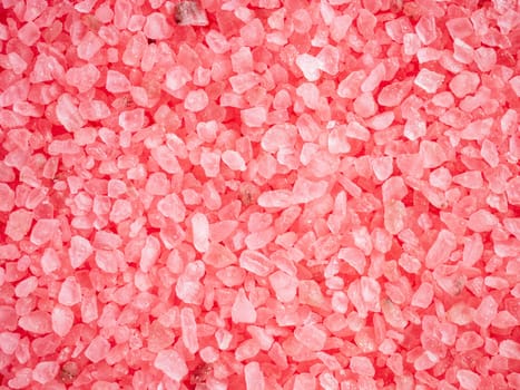 Beauty and body care concept. Pink colored salt crystals as a background. Aromatic roseate bath salt with litchi and patchouli scent. Large sprinkled crystals of crimson sea salt. Close up.
