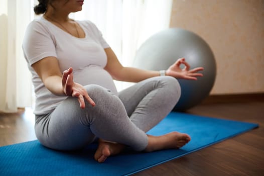 Close-up pregnant woman yogi holding fingers in mudra gesture, meditating, reaching zen, balance and harmony, feeling calm, positive and relaxed. Yoga practice. Meditation for healthy active pregnancy