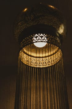 Traditional Oriental lamp. Lacy metal Arabic hanging lamp with long chains. Concept for Moroccan and Arabian culture and design. Rich golden chandelier. Vertical view. Soft focus.