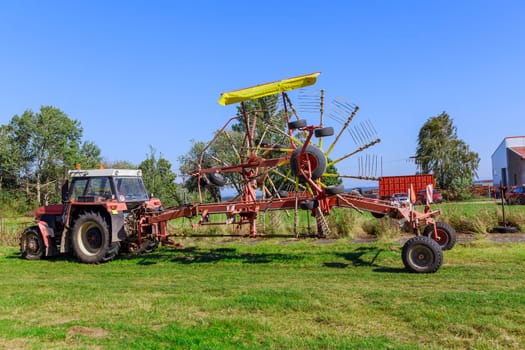 Tractor to which rake of stirrer is attached. With help of tractor, farmer pressed hay in high-quality manner, ensuring good supply for year.